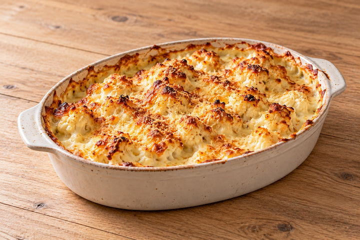 Gratin de chou-fleur doré dans un plat en céramique, béchamel au comté gratinée, quelques bouquets qui dépassent
