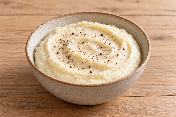 Purée de chou-fleur lisse et blanche dans un bol en grès, un tour de poivre noir sur le dessus