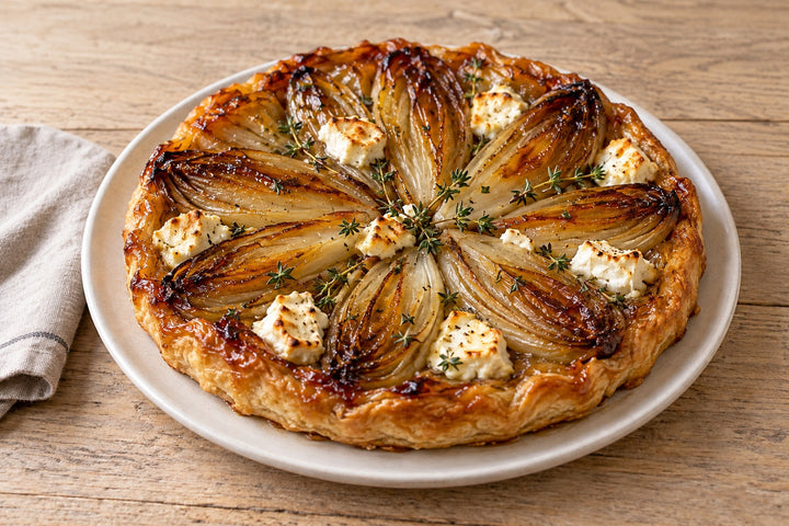 Tarte tatin aux endives retournée sur un plat, endives caramélisées et brillantes, chèvre fondu et thym